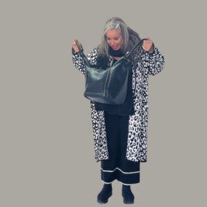 Frau mit grauen Haaren trägt einen schwarz weißen Strickmantel und schaut erfreut in eine modische Handtasche